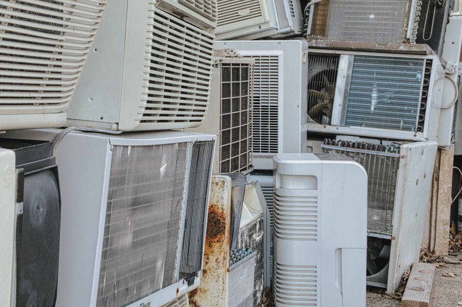 A collection of discarded household appliances stacked against a wall, including a white washing machine with visible dirt marks and rust around the door surround, a white dryer with signs of weatheri